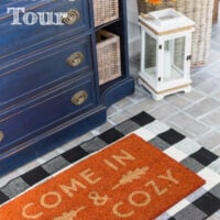 Blue sideboard in fall decorated foyer with a rug that says come in and get cozy