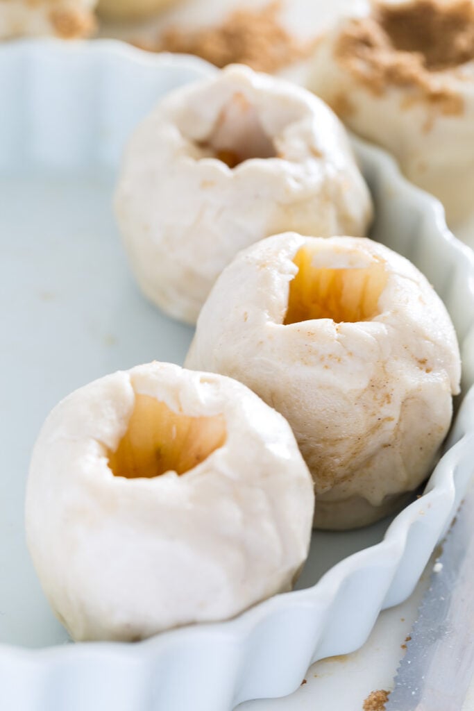 Cored apples wrapped in pastry in a baking dish.