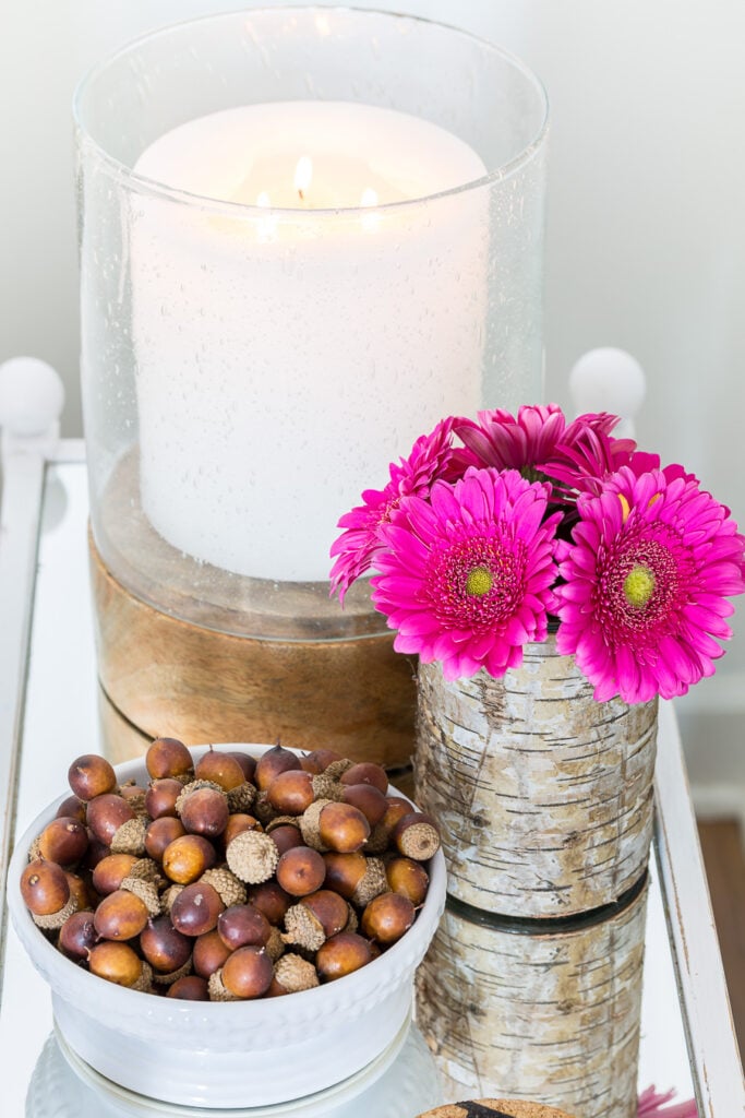 Pretty pink flowers on mirror table with a white candle and a bowlful of acorns.