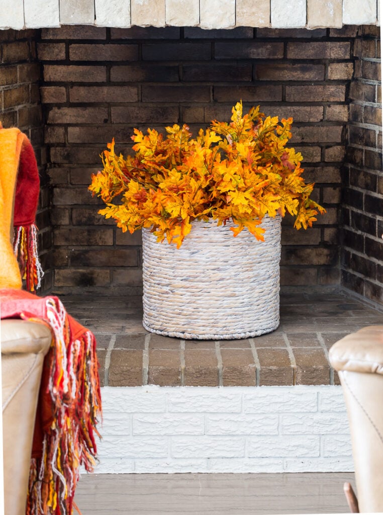 Fall leaves in basket placed in an unused fireplace.