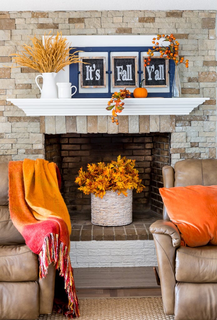 Fall leaves in basket placed in an unused fireplace flanked by 2 leather recliner chairs.