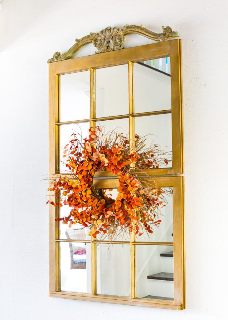 2 window sashes mounted on a wall to create a tall wall mirror. Fall wreath on center.