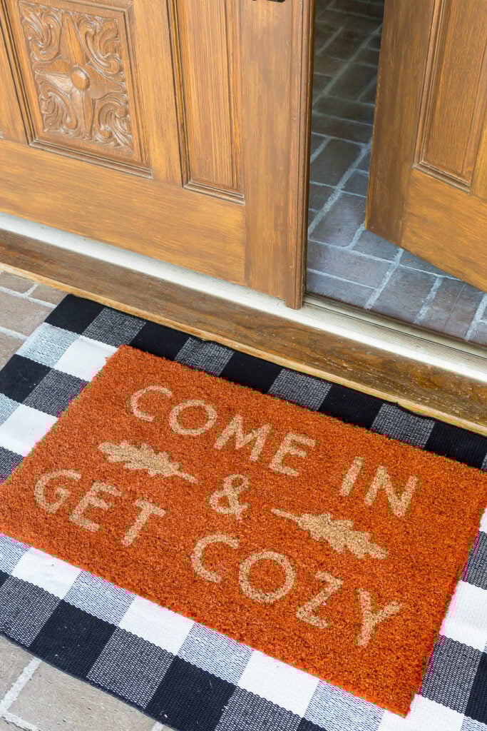 Come in and get cozy orange fall door mat on a homes front porch entry