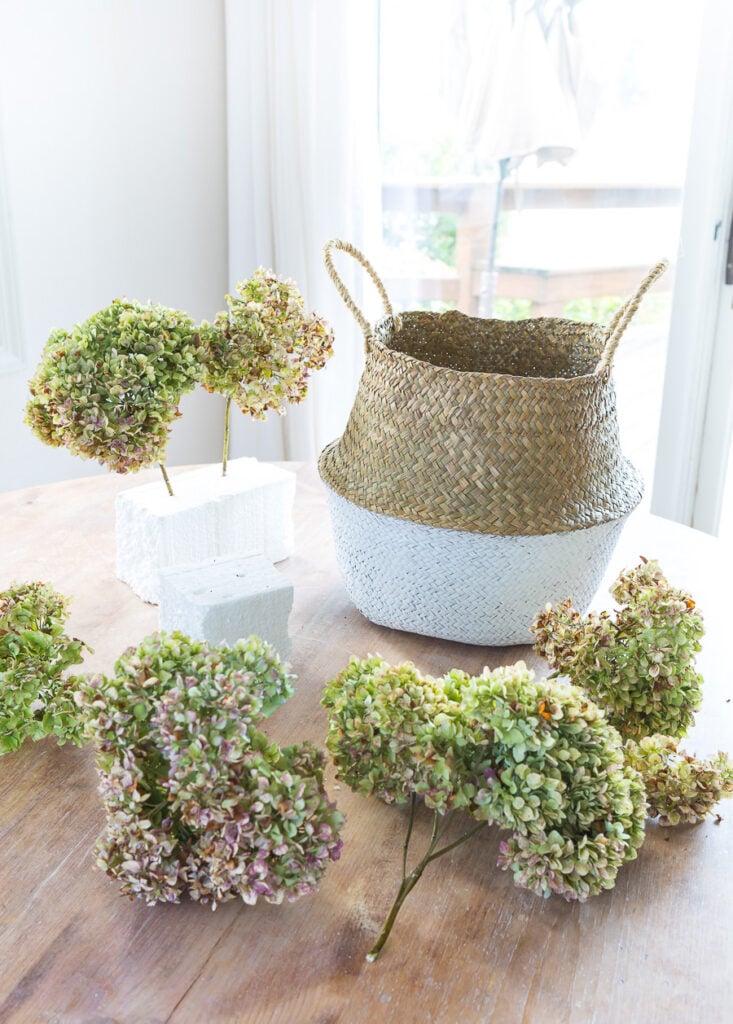 Dried hydrangeas and collapsible rattan tote on table getting ready to create a floral arrangement.