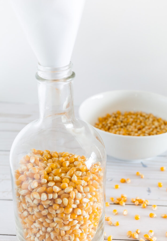 how to pour popcorn into a glass bottle with a narrow neck using a paper funnel to make a fall candle holder.