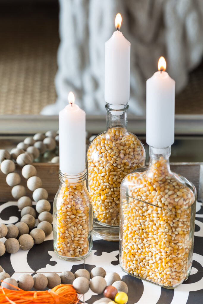 3 glass bottles filled with popcorn and then a candle placed into the bottles opening make for budget friendly fall decor. 