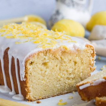 Close up of the end of a sliced vegan lemon drizzle loaf cake topped with lemon glaze and sugared lemon zest.