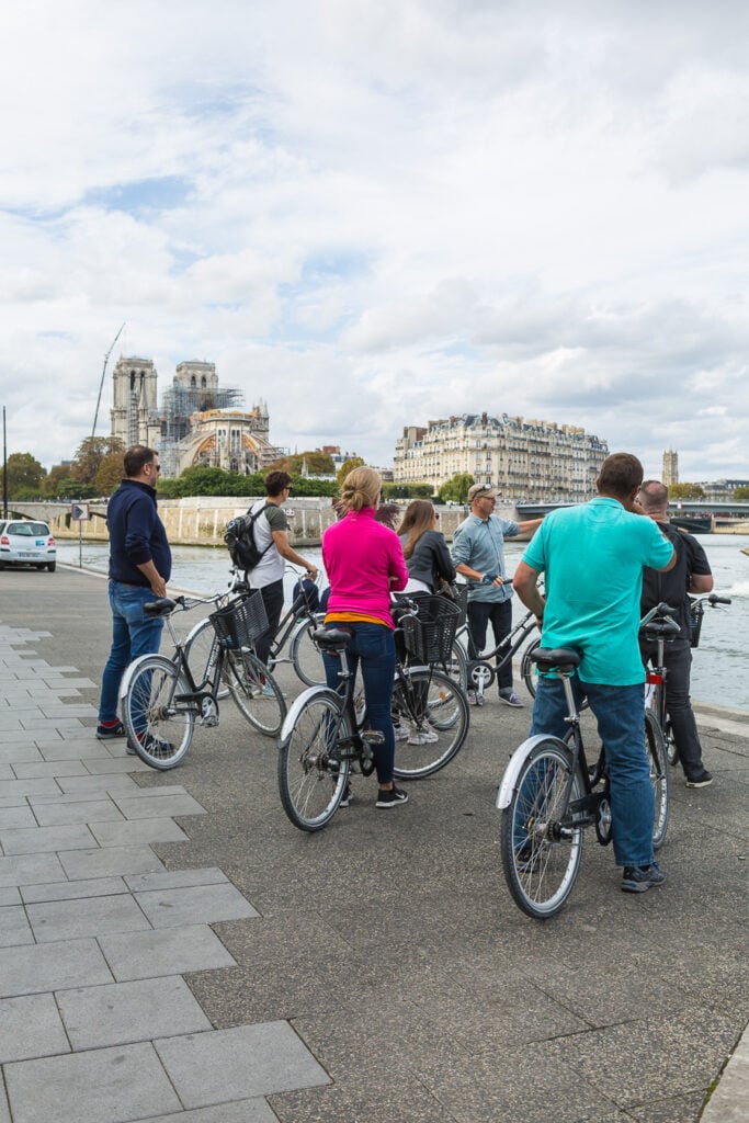 Bicycle riders on a tour through Paris stopping along the Seine in Paris to listen to a tour guide.