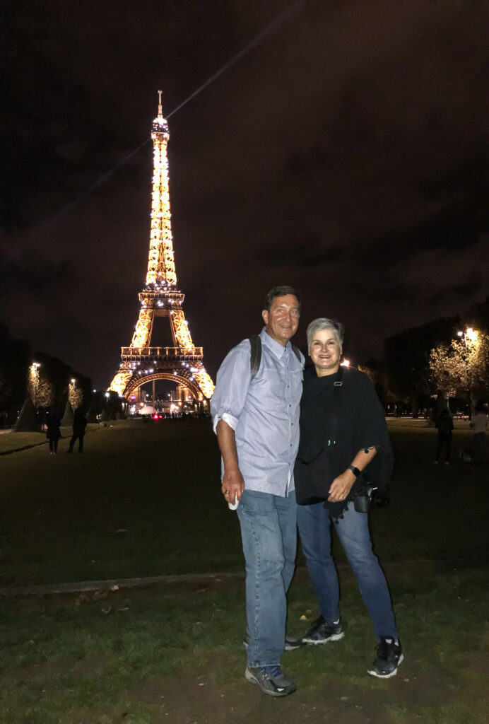 Blogger Diane Henkler and Ed standing in front of the Eiffel Tower at night when it was lit and twinkling. They were on a Paris bike tour at night.