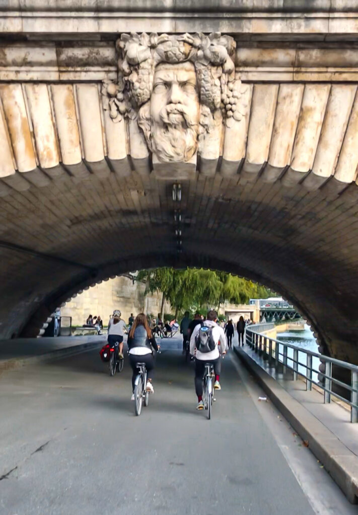 Riding in a bike tour group in Paris under a bridge along the Seine with Bike About Tours Paris.