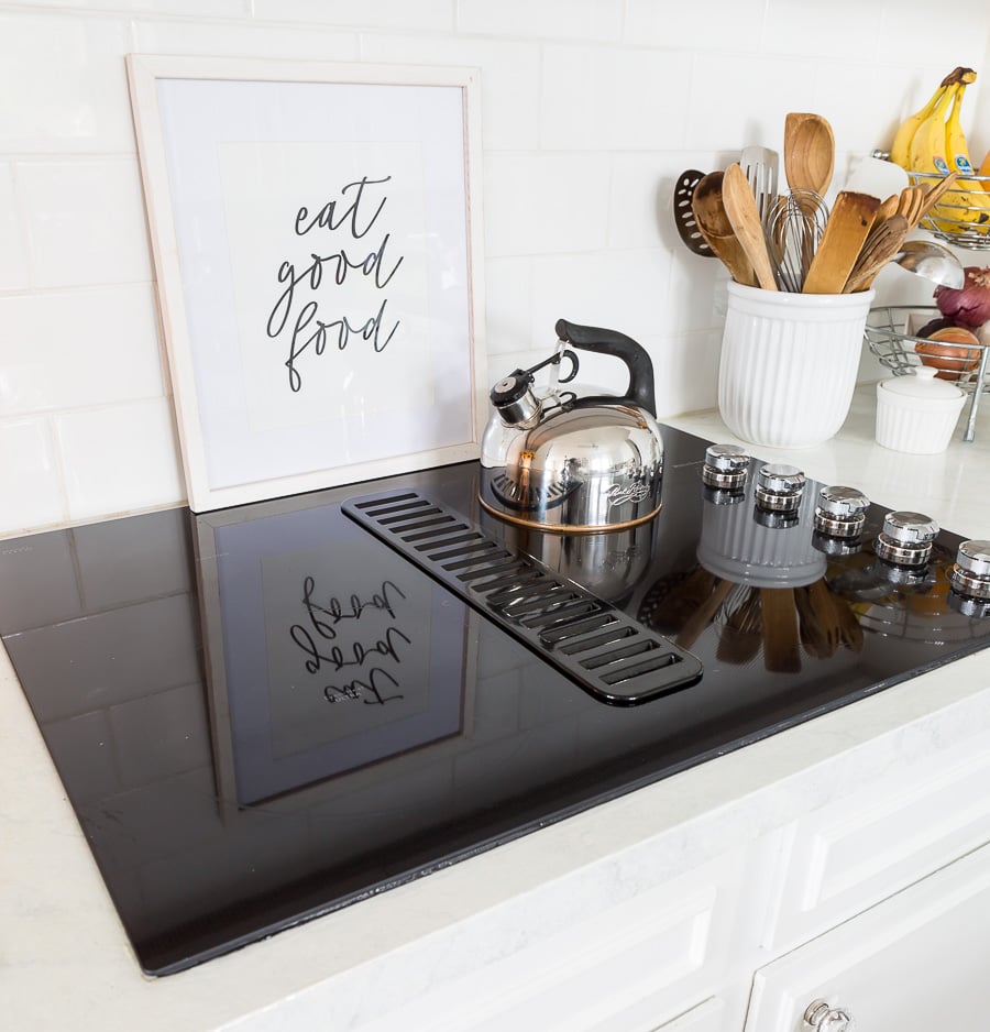 New black ceramic cooktop in white kitchen. Art leaning against back splash that says, Eat Good Food
