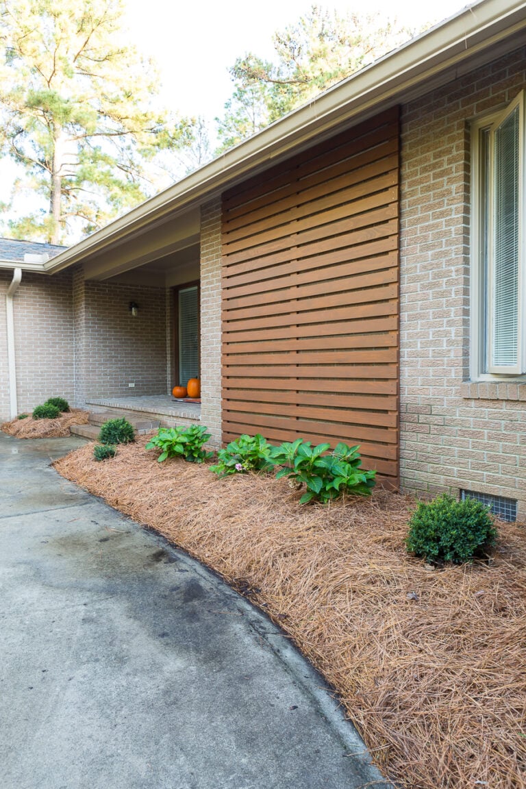 After photo showing stained outdoor modern wood slat accent wall on brick Ranch home.