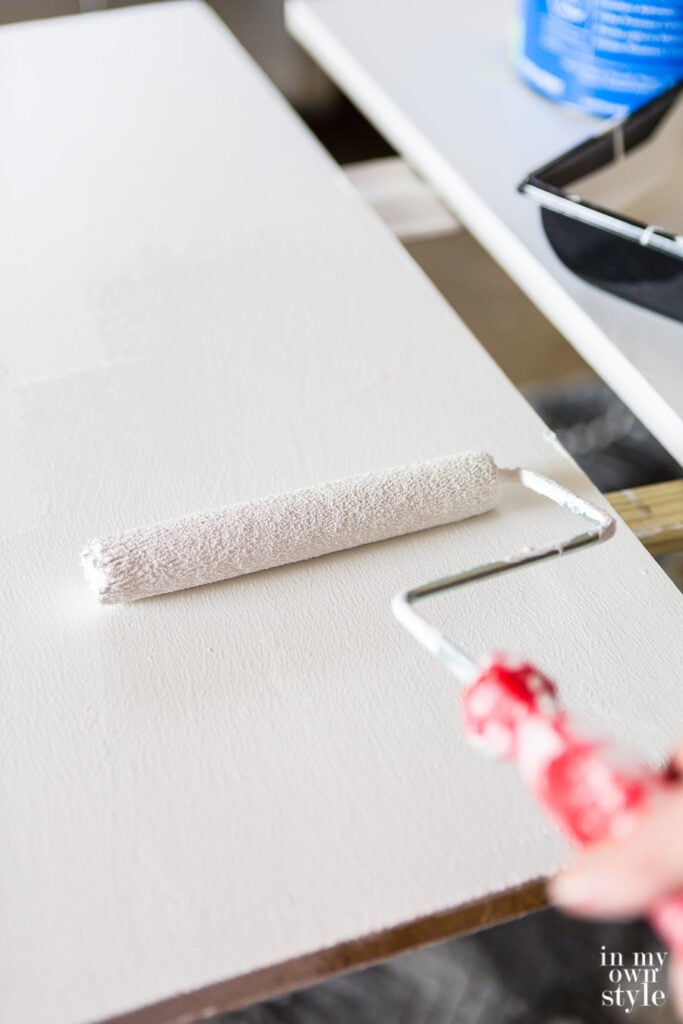 Rolling white paint on wood shelves over a primer coat