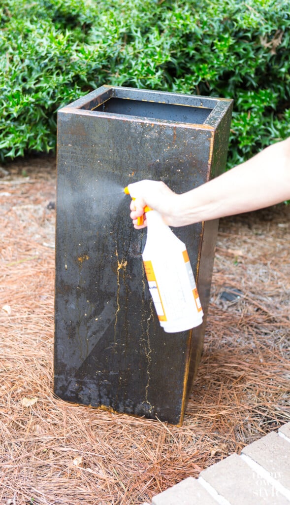 First coat of rust accelerator being applied with a spray bottle on surface of metal planter.