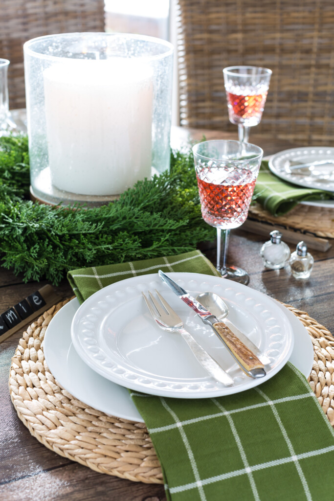 Round dining table set for a Christmas dinner using white plates and olive green napkins