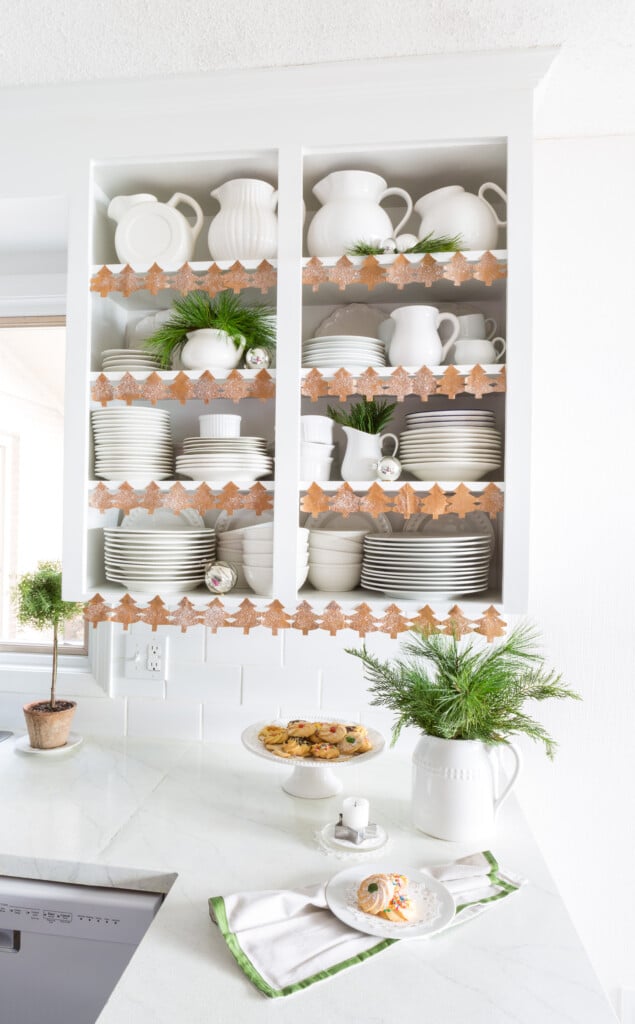 Kitchen decorated for Christmas. Open shelfs trimmed with a cutout paper chain of pine tree shapes.