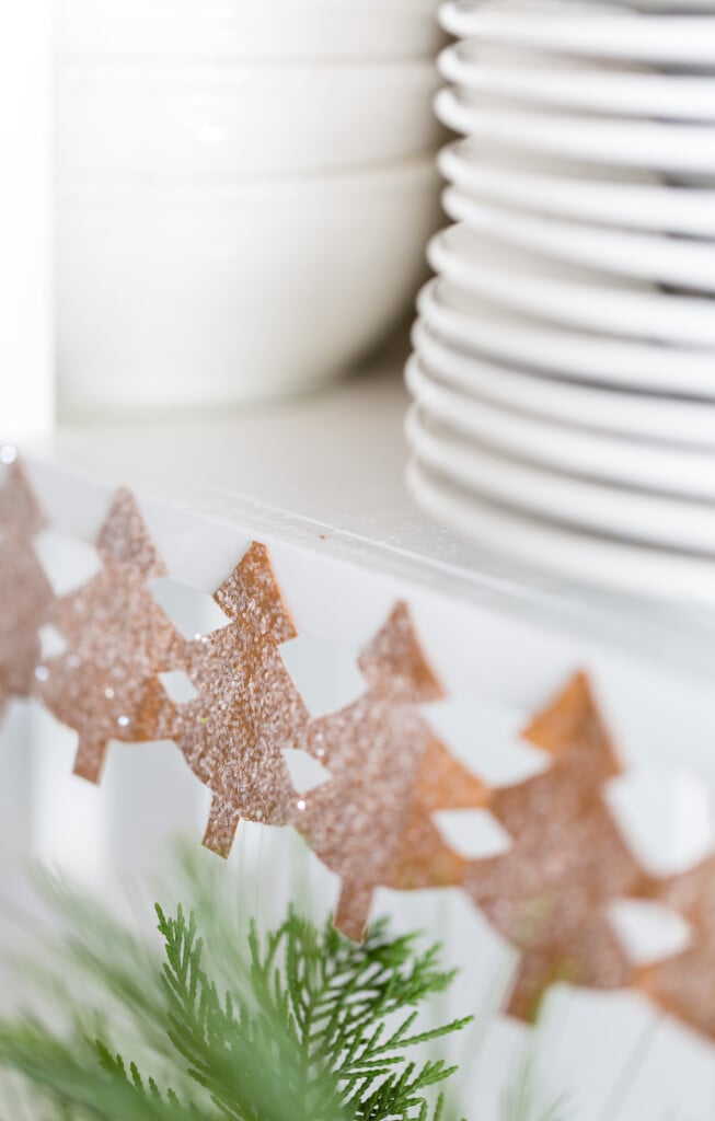 Close up image of a paper chain of pine trees decorating the edge of kitchen shelves for the holidays.