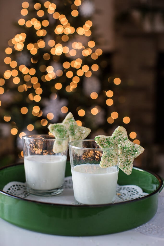 Two star shaped cookies  sitting on the rims of milk filled drinking glasses.