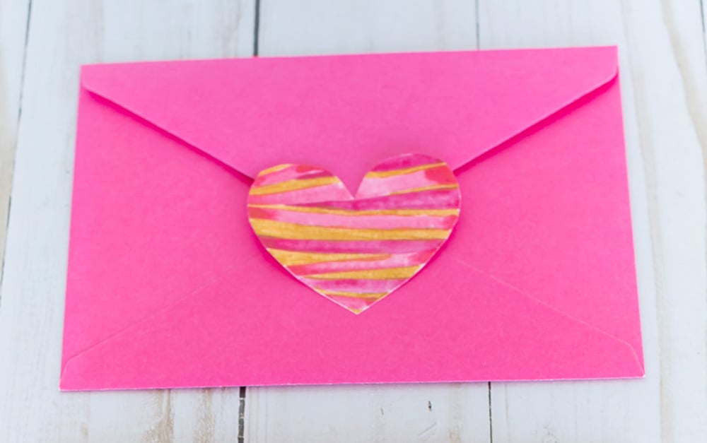 Valentine heart paper cutout glued to the flap of a pink envelope.