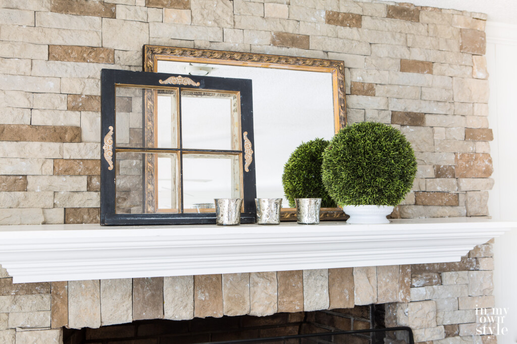 A mantel styled for the winter using a small wood window frame that was painted black and gold.