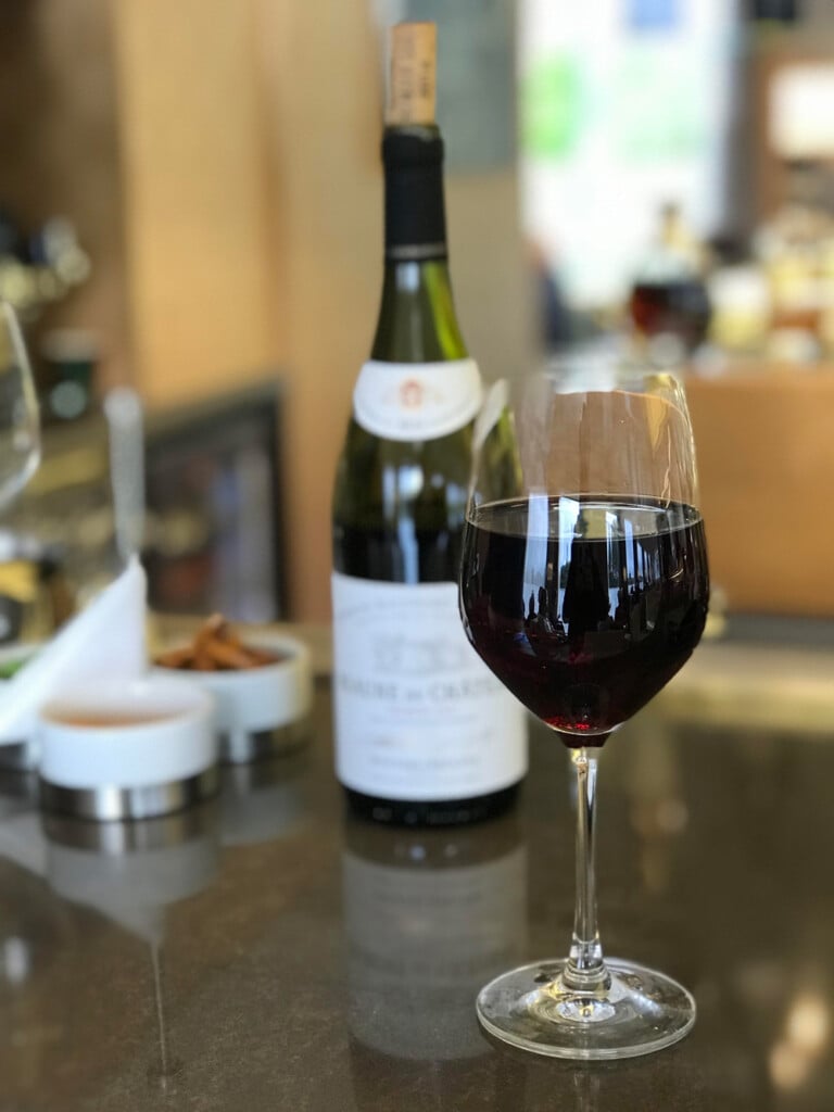 glass of red wine on counter with bottle behind it