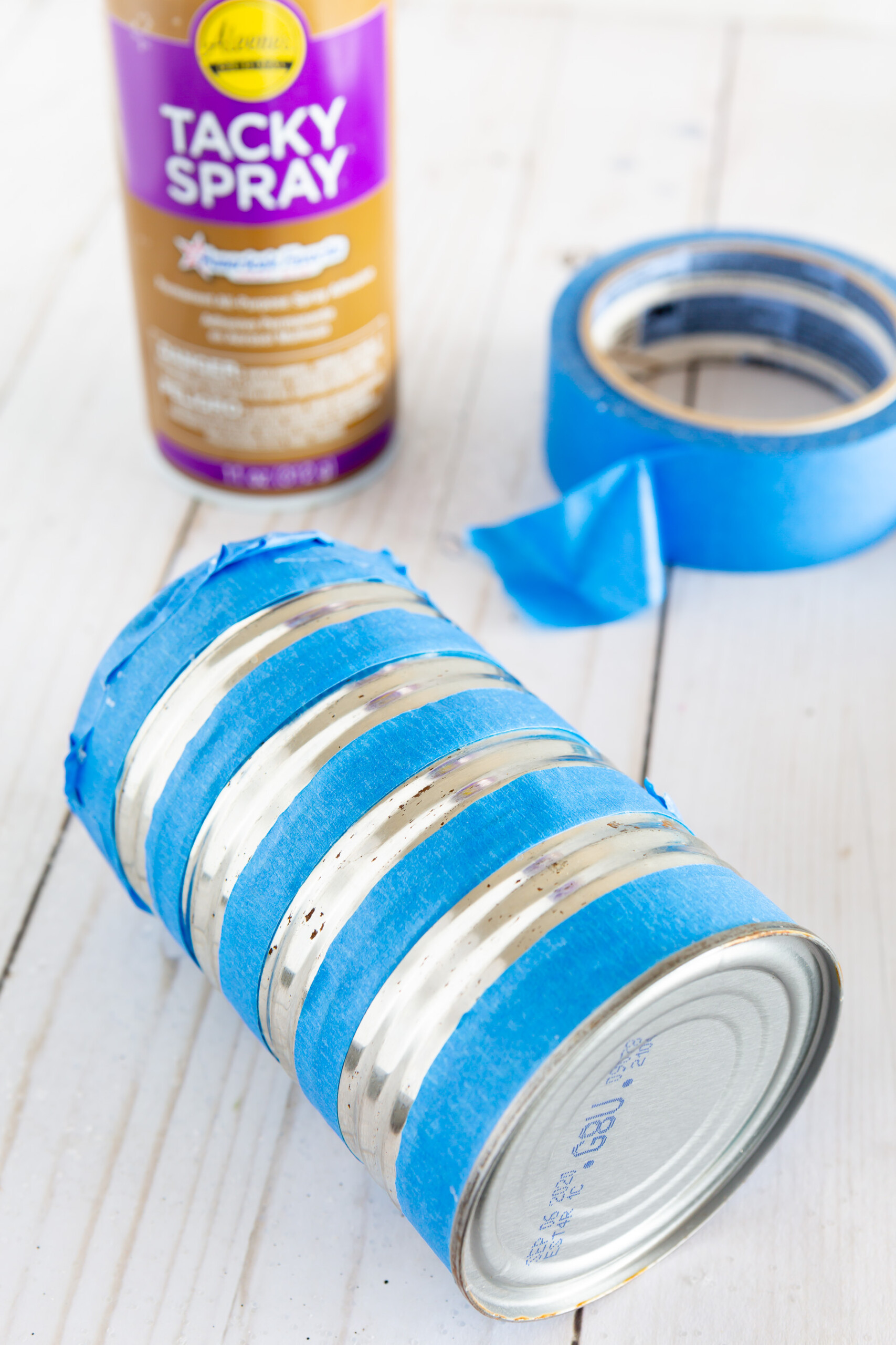 applying tape to a tin can to create glitter stripes to make a vase.