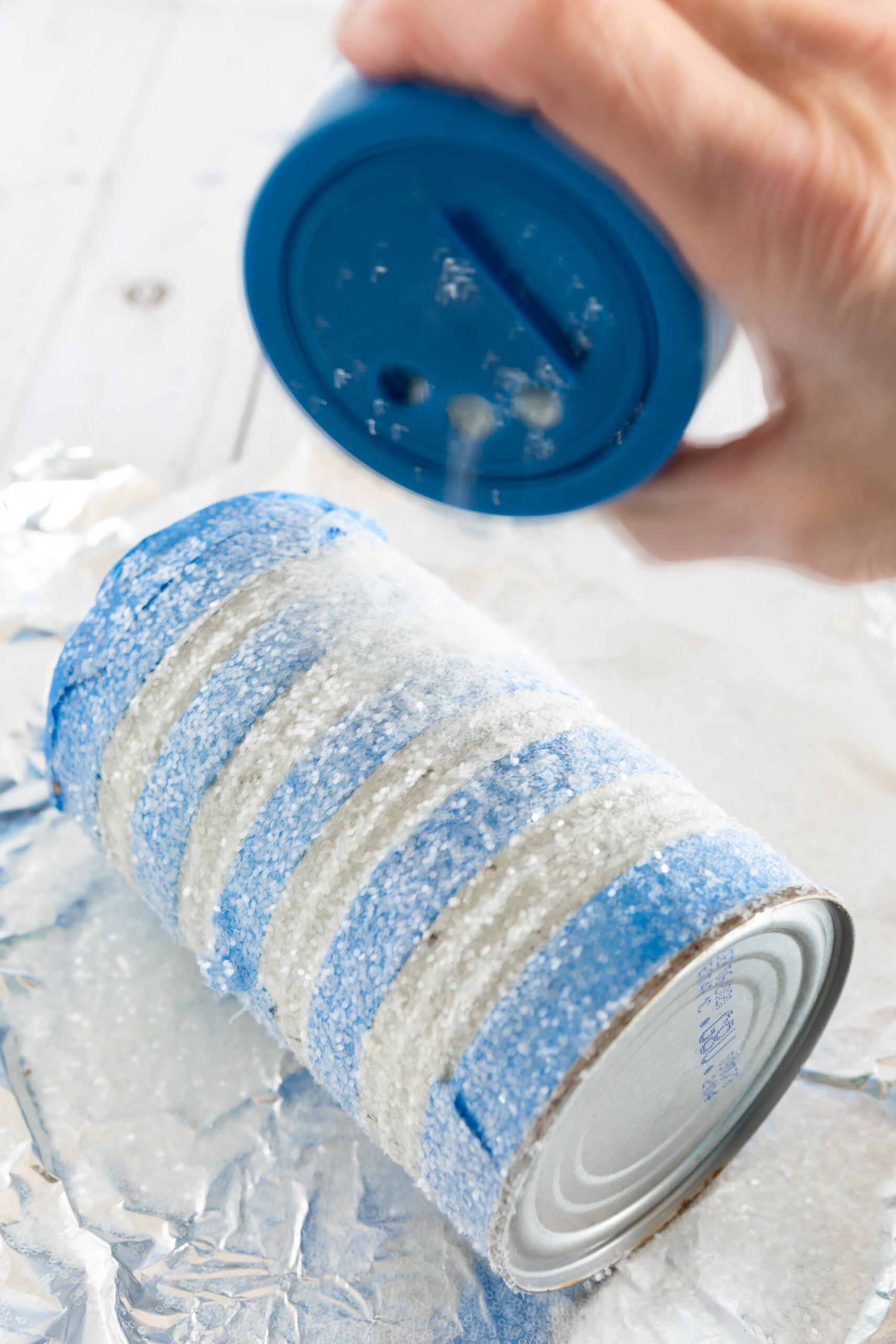 applying glitter to a tin can to make a pretty vase or centerpiece on a budget