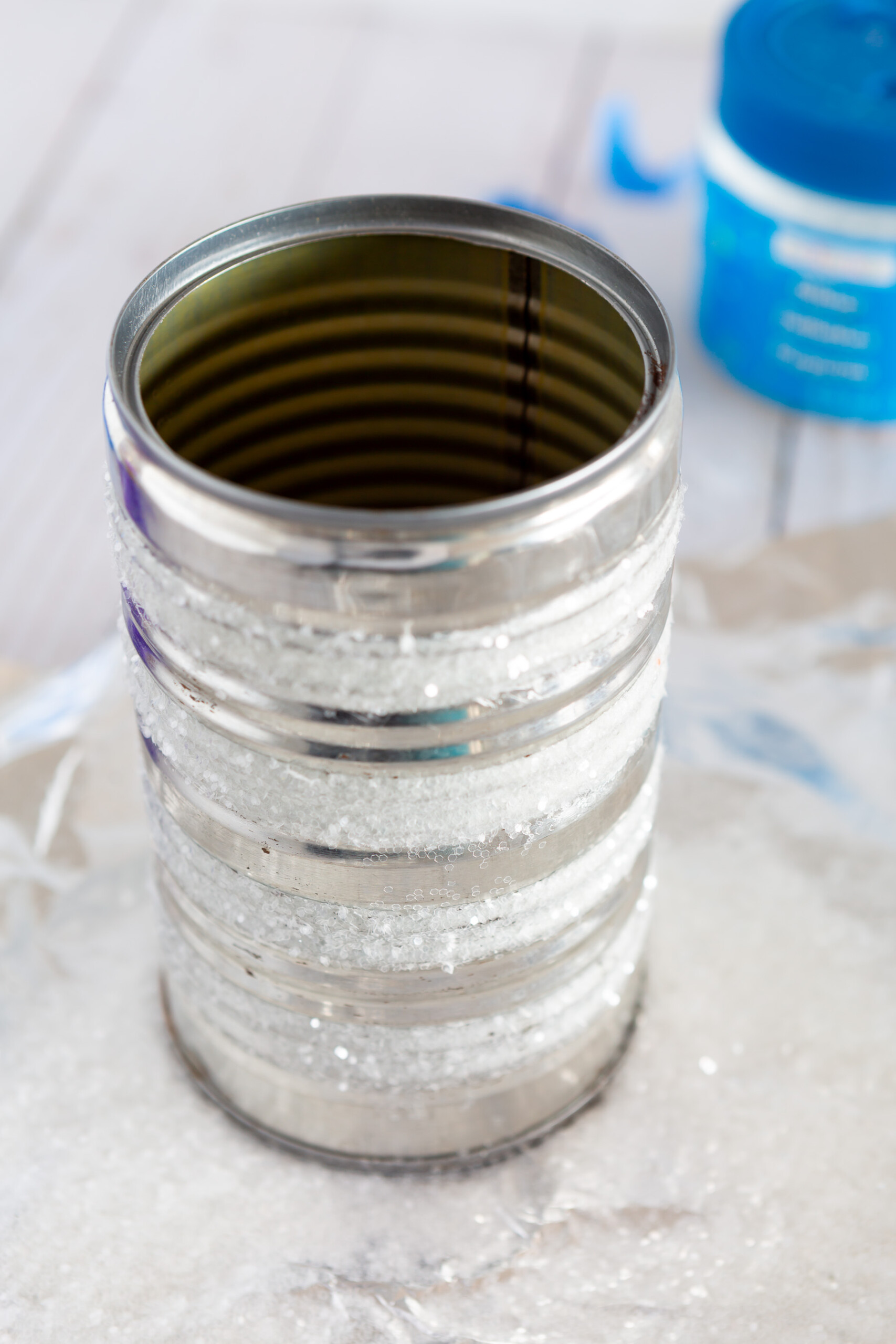 how to steps showing how to add stripes of glitter on a tin can to make a pretty vase for a kitchen counter.
