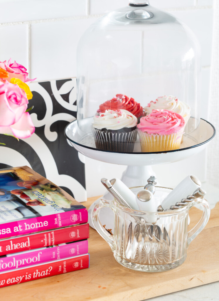 cupcakes under a glass dome cake stand on a kitchen counter.