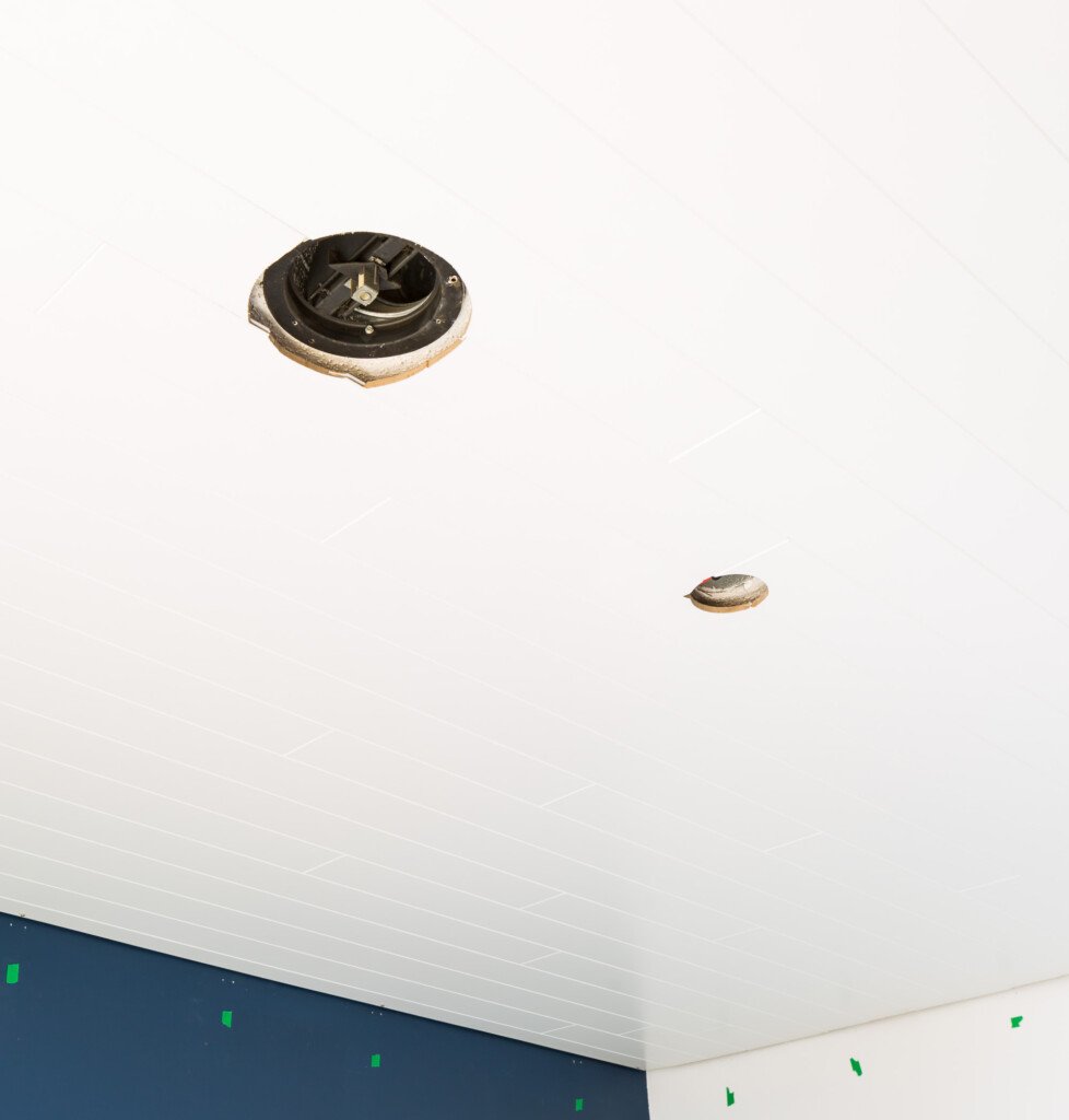 Newly white plank covered ceiling showing circular cutouts where light fixture and HVAC vent will added. 