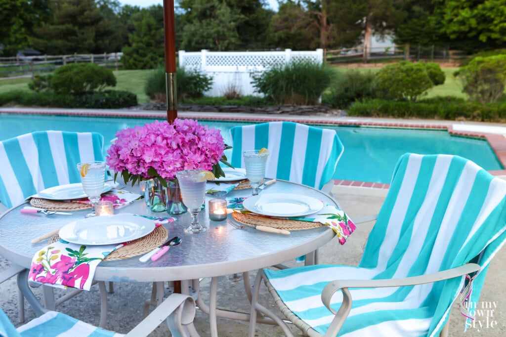 Centerpiece vase for patio table with an umbrella. White and teal striped beach towels on chairs used as casual but coloful covers.