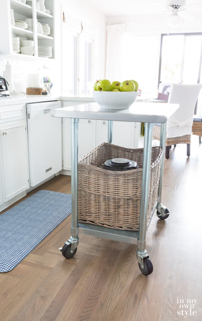 Metal rolling kitchen island with large rattan basket on bottom shelf.