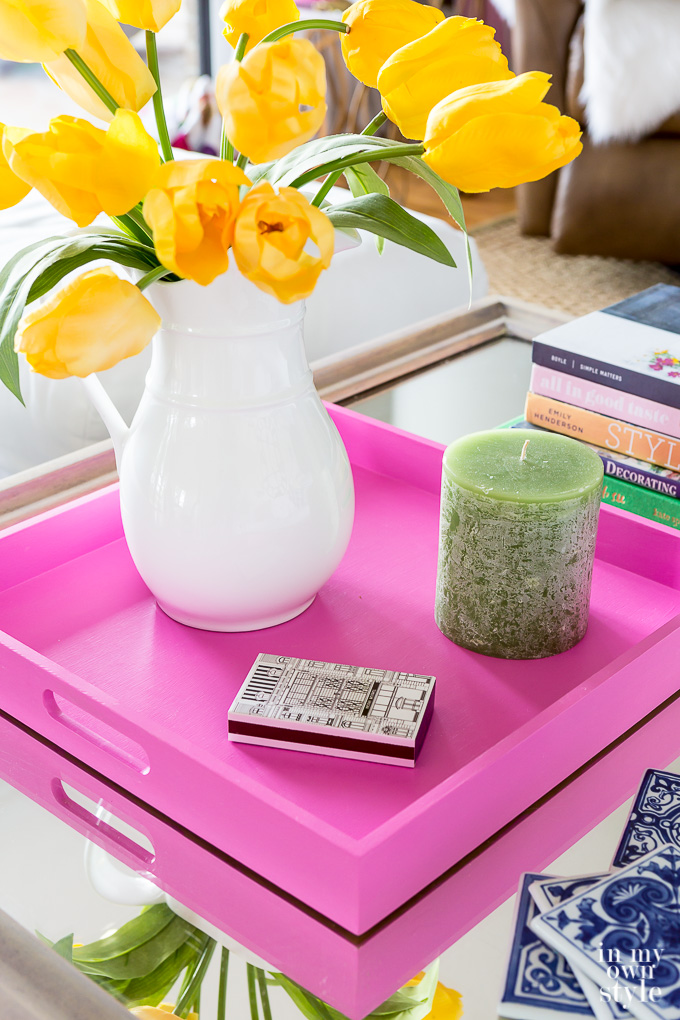 Coffee table with a pink wooden tray with yellow tulips and a candle on it.
