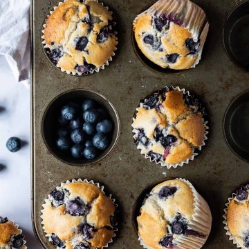 vegan blueberry muffins in a metal muffin tray with fresh blueberries on a marble background.
