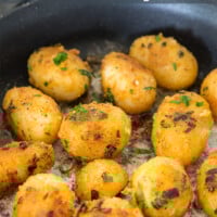 Canned whole potatoes covered with seasoning cooking in skillet.