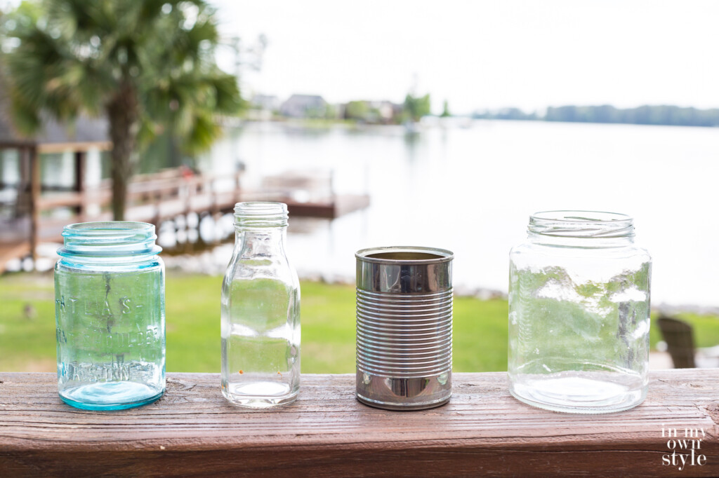 Saved from the recycling bin. Glass jars and a tin can lined up on an outdoor deck railing.