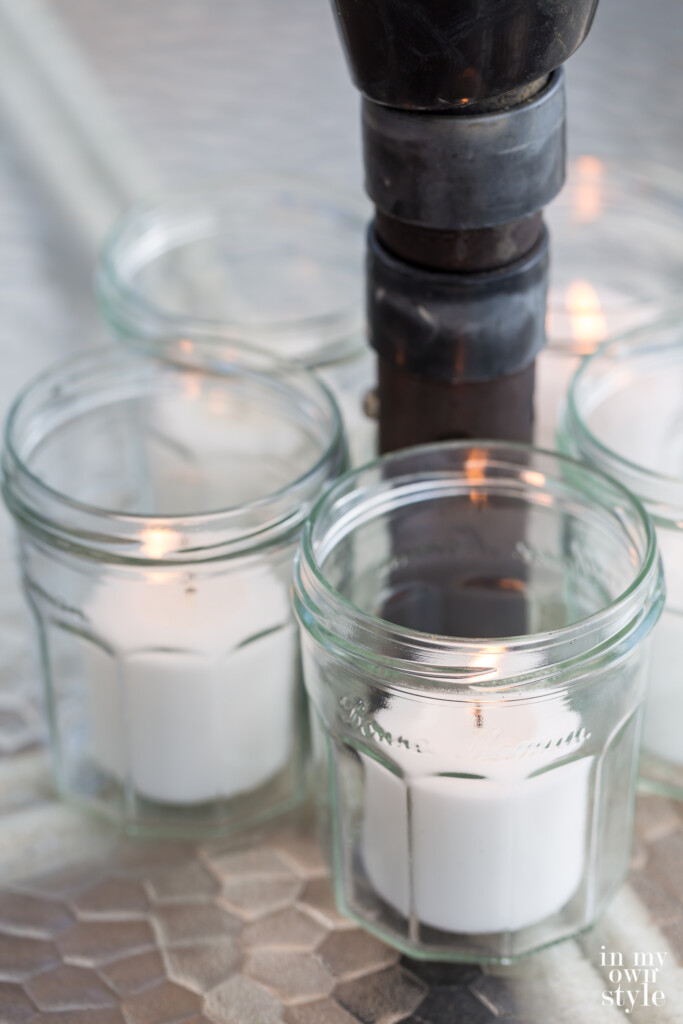 Jelly jars with candles in them around an umbrella pole on a dining table.