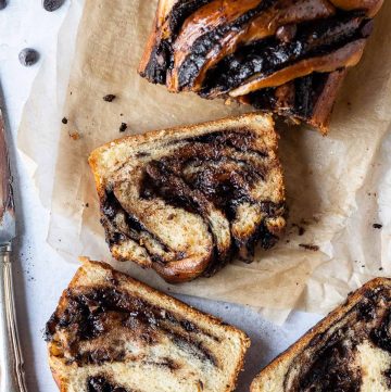 Sliced vegan chocolate babka on brown baking parchment on a grey background.