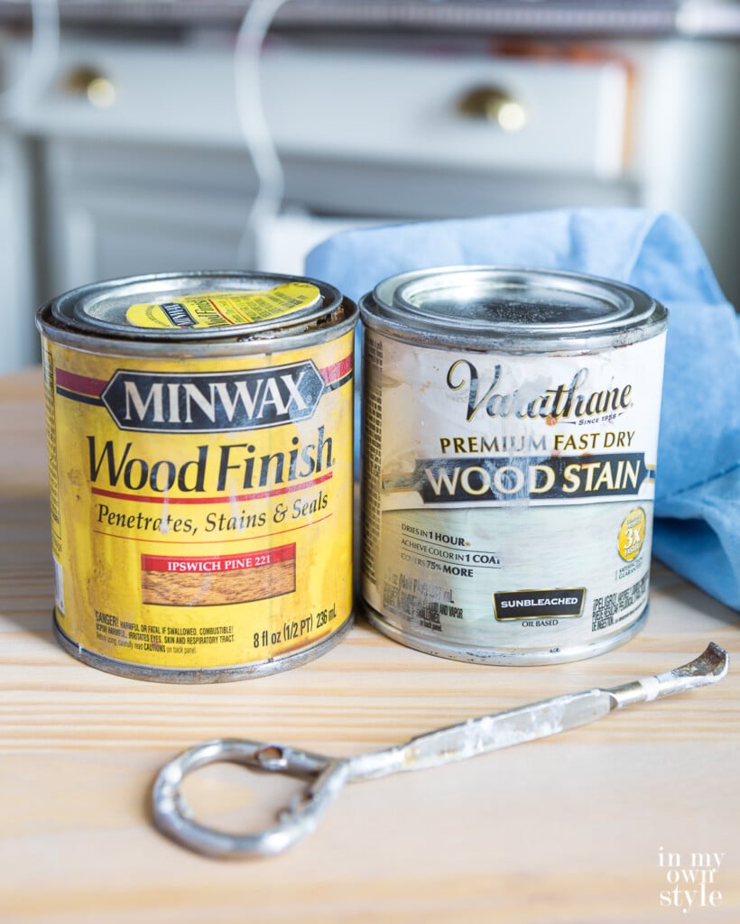 Two cans of stain and opener on table. Minwax Pecan and Varathane Sunbleached