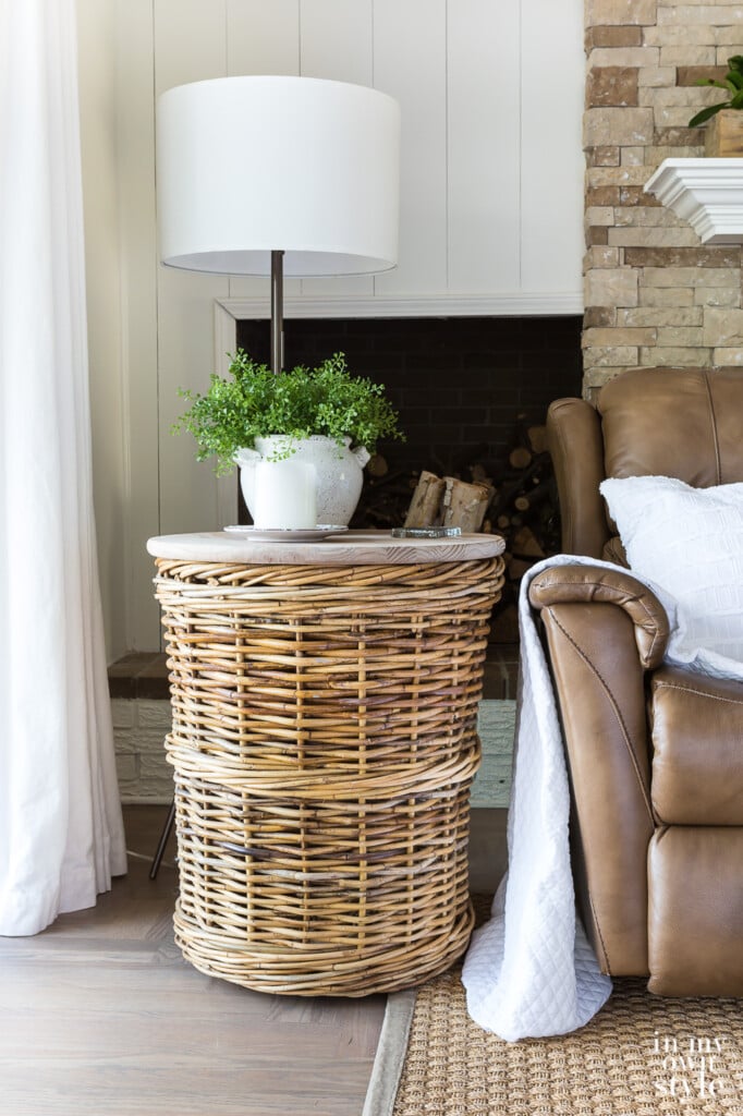 Large basket made into a diy end table. It sits next to a brown chair with a white throw and pollow.