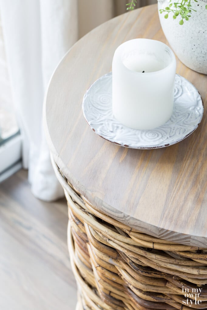 Looking down at the wood top of a basket side table. Candle on plate on top.