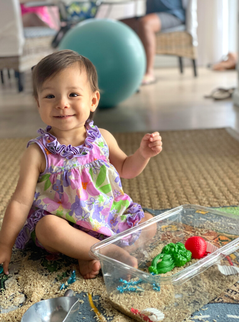 Grand baby sitting on floor playing with a box of toys.