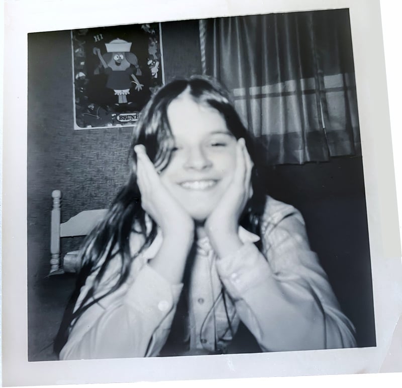 Diane-in an old black and white photos at-around-12-years-old laying on a bed with hands under my chin.