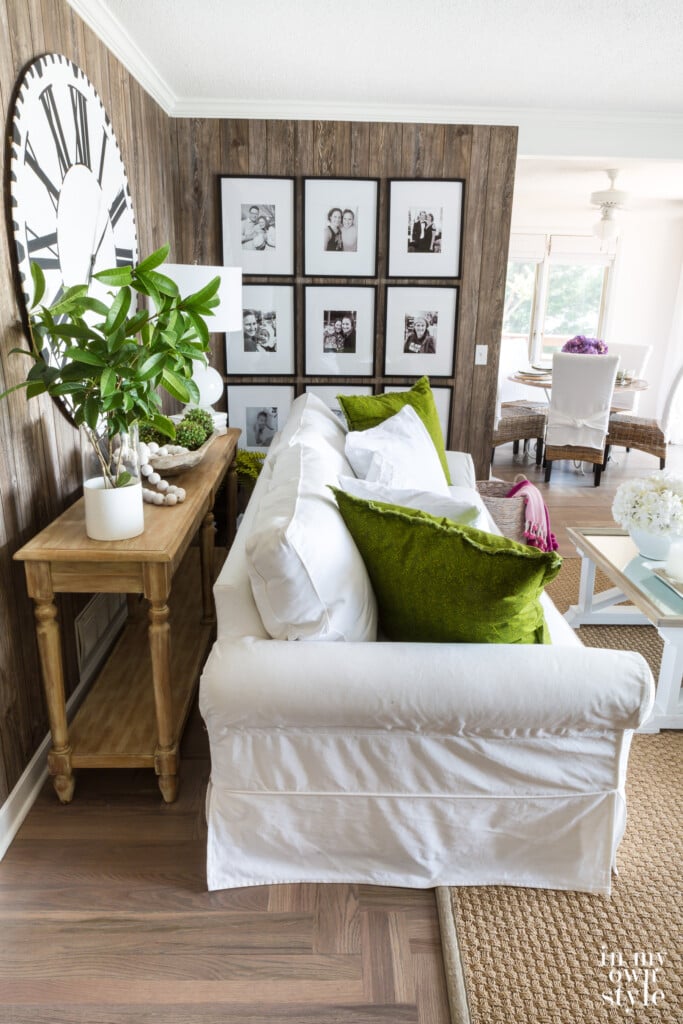 Faux barnwood paneled wall in living room with photo gallery, white sofa with green pillows and seagrass rug.