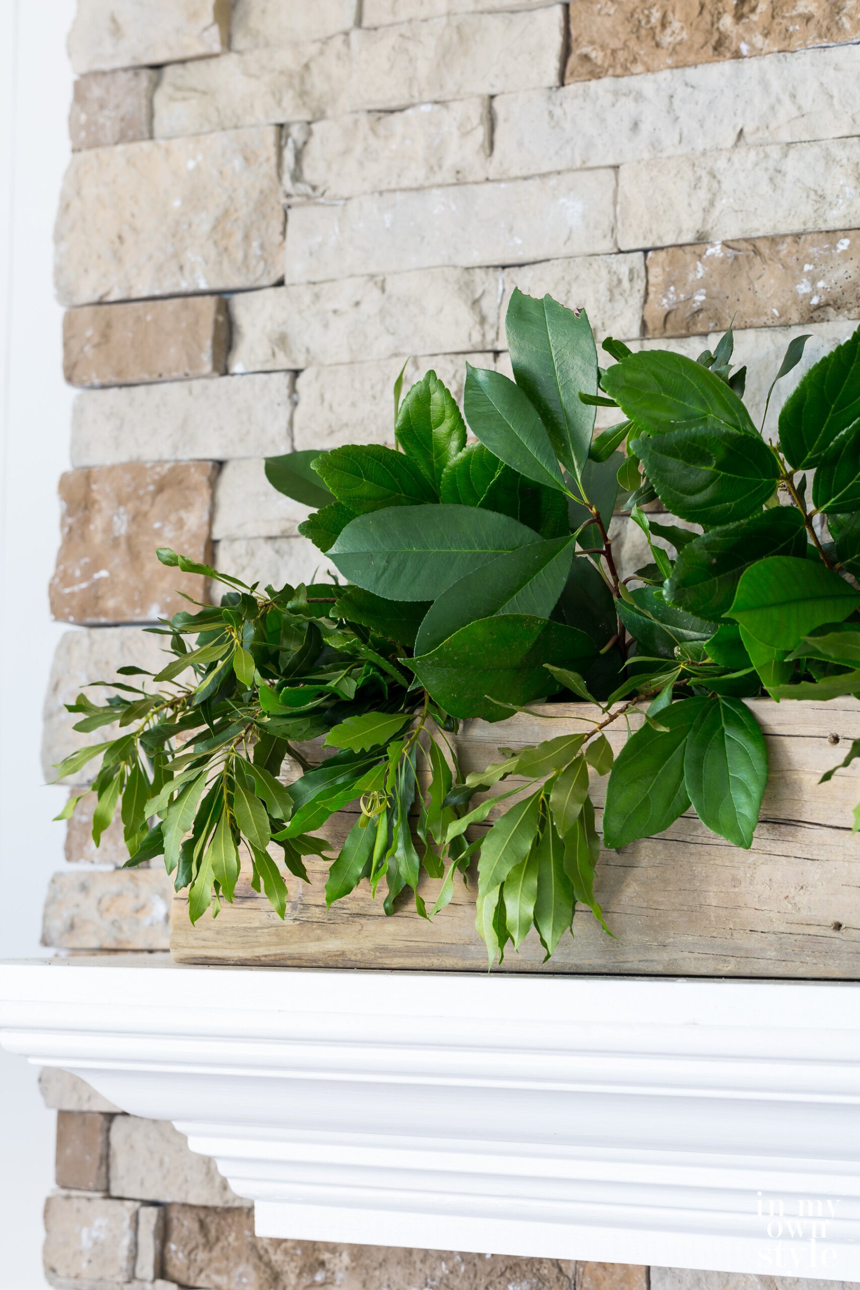 Long sun weathered wood planter on top of mantel filled with shrub clippings.