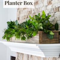 Stone fireplace with white mantel. Wood planter box filled with greenery on top. Text overlay says Easy DIY mantel planter box.