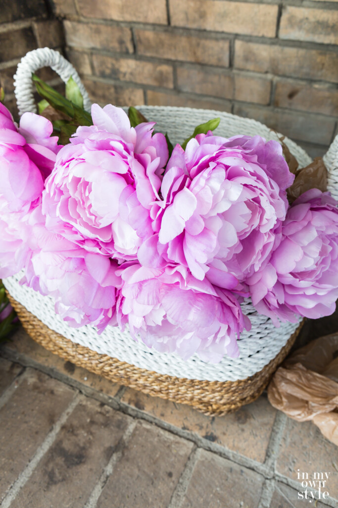 Faux pink peonies in a large basket that is placed in an empty fireplace for summer decorating.