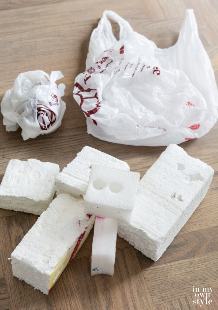 Foam pieces and plastic bags on floor that will be used to fill a large basket before faux flower stems are placed in.