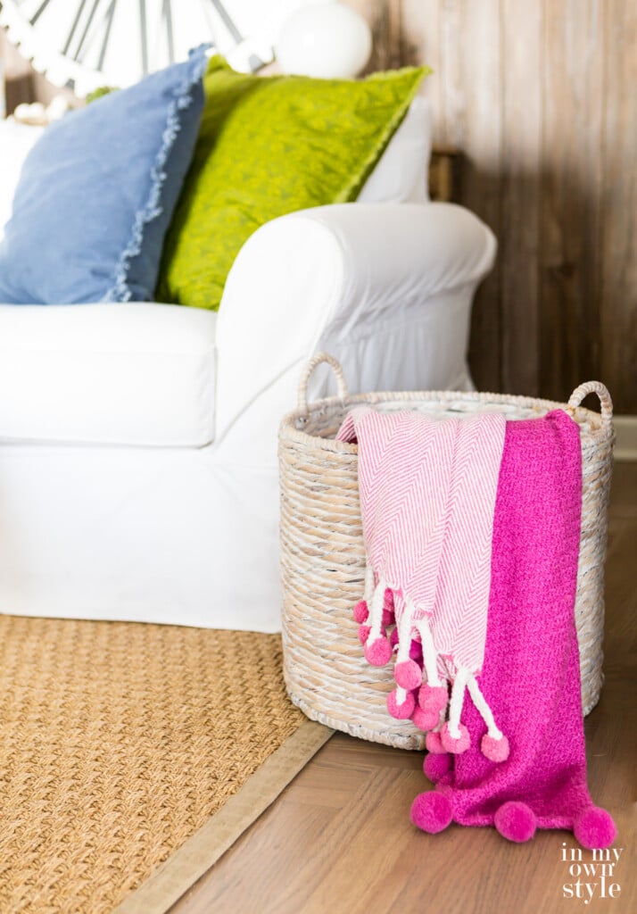 Large floor basket in living room with two throw blankets hanging over the side.