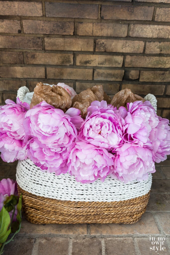 Large basket getting filled with faux pink peonies using plastic bags as filler to make the basket look filled.
